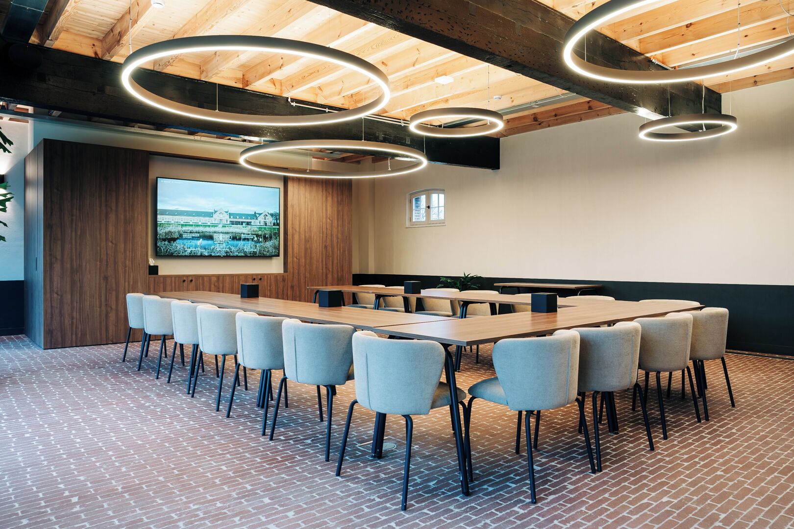 A conference room with a long table, multiple chairs, and a large screen on the wall.