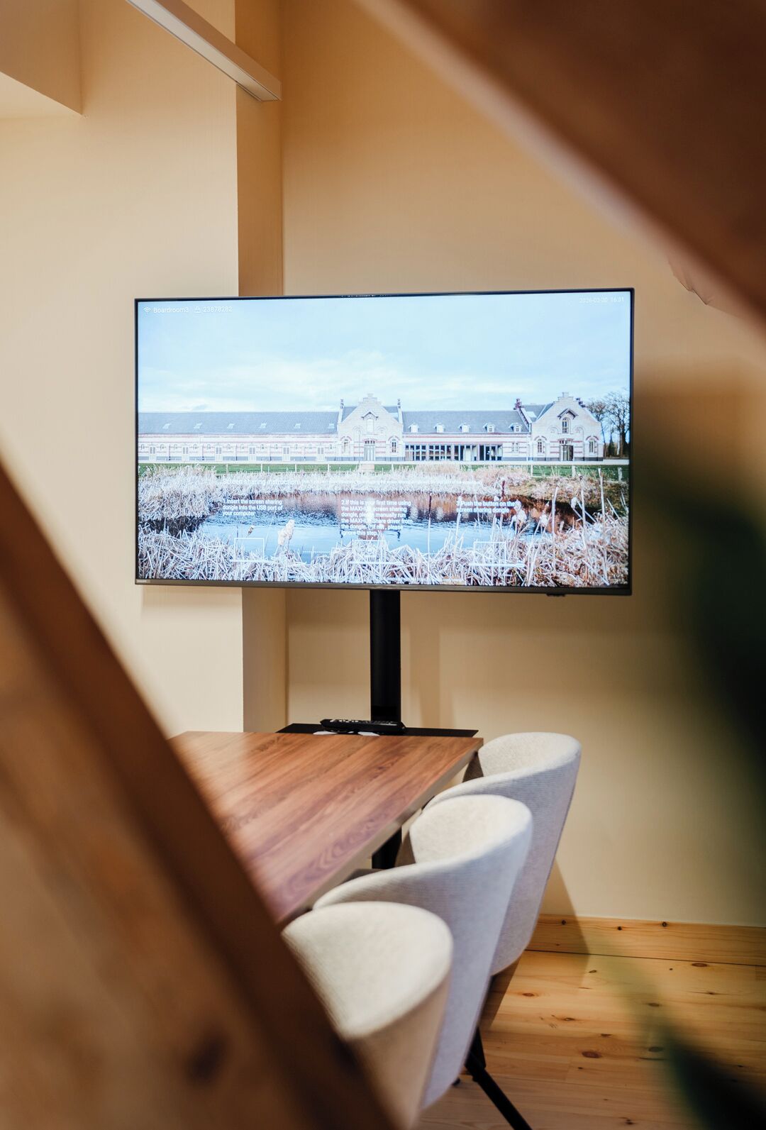 Een televisie aan de wand, toont een landschappelijk uitzicht op een gebouw en een waterlichaam.