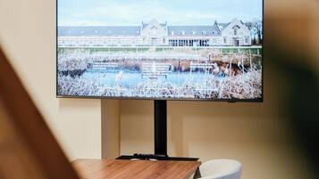 Een televisie aan de wand, toont een landschappelijk uitzicht op een gebouw en een waterlichaam.