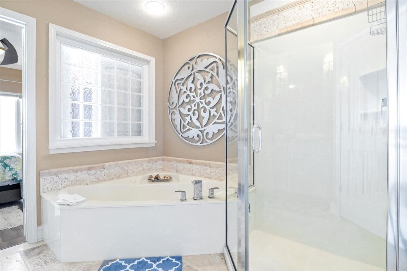 A bathroom with a bathtub, a glass shower enclosure, a decorative wall piece, and a window.
