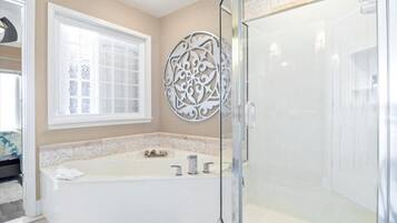 A bathroom with a bathtub, a glass shower enclosure, a decorative wall piece, and a window.