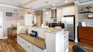 A kitchen with a central island, white cabinetry, stainless steel appliances, and a seating area with a bench. - Heavenly Hideaway - 2 Pools, Hot Tub, & More! (Lake Ozark)