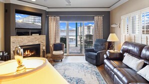 A living room with a fireplace, a sofa, a chair, and a TV. - Heavenly Hideaway - 2 Pools, Hot Tub, & More! (Lake Ozark)