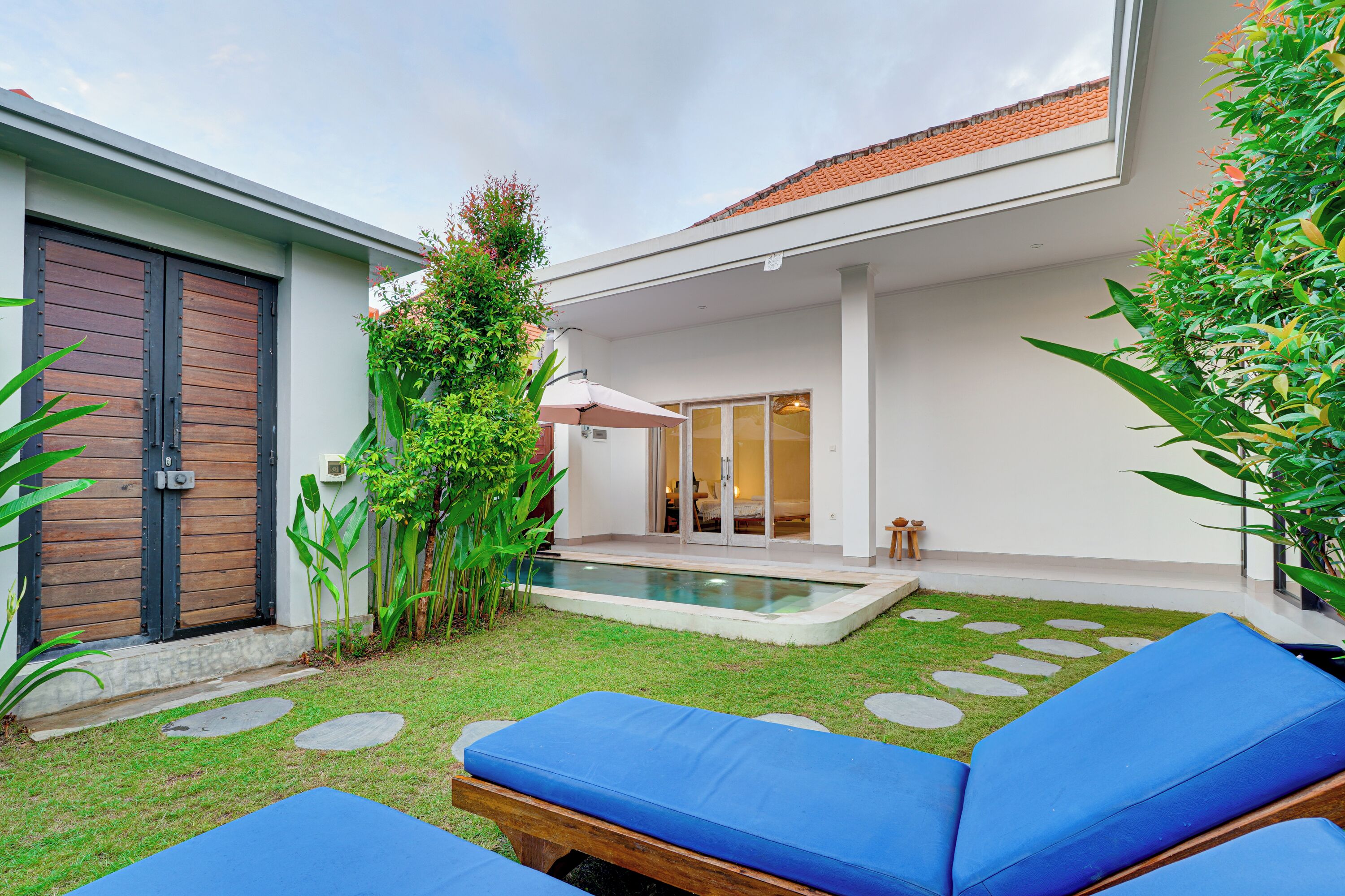 A modern house with a swimming pool, blue lounge chairs, and a well-maintained garden.