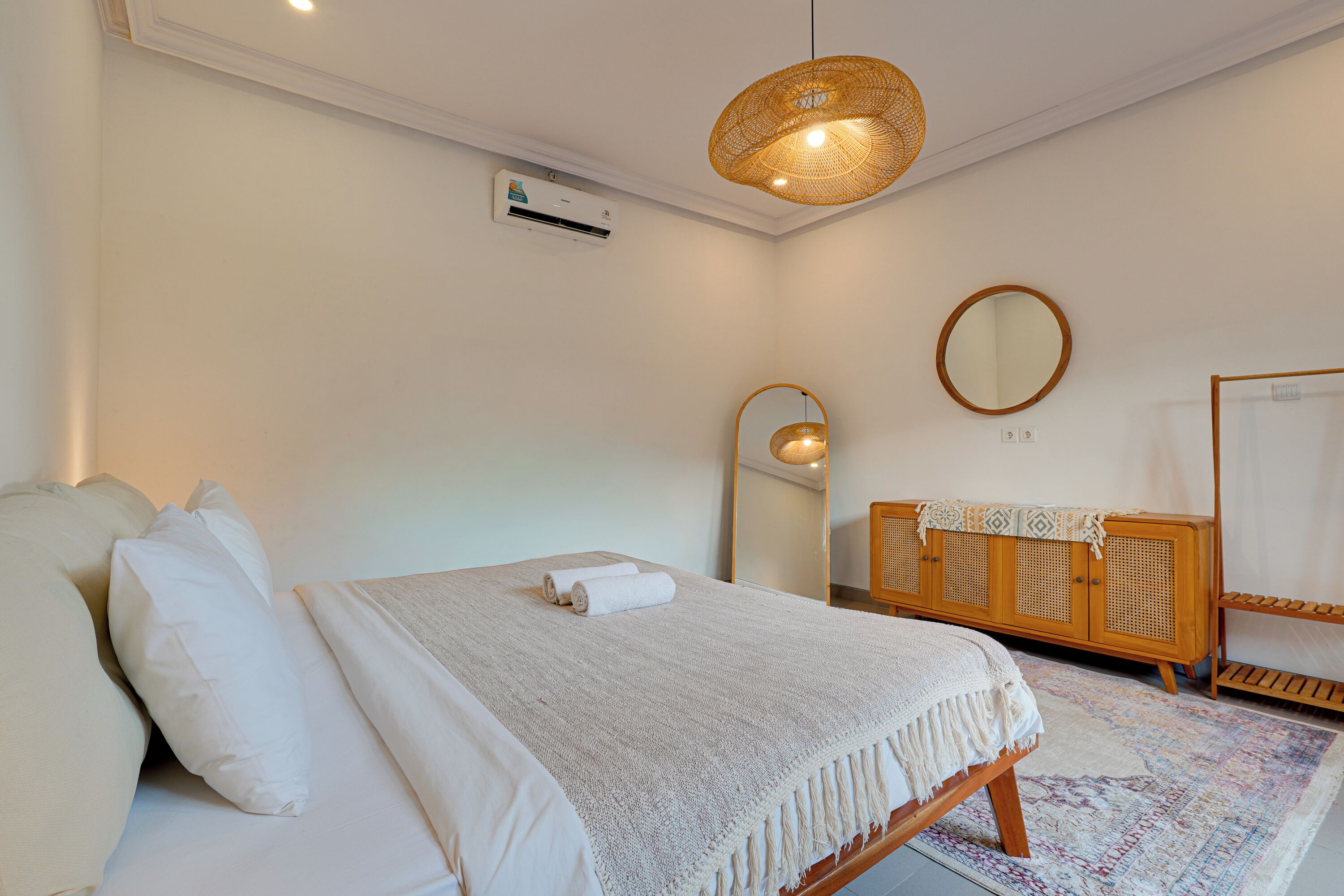A bedroom with a bed, a bedside table, a mirror, and a wooden dresser.