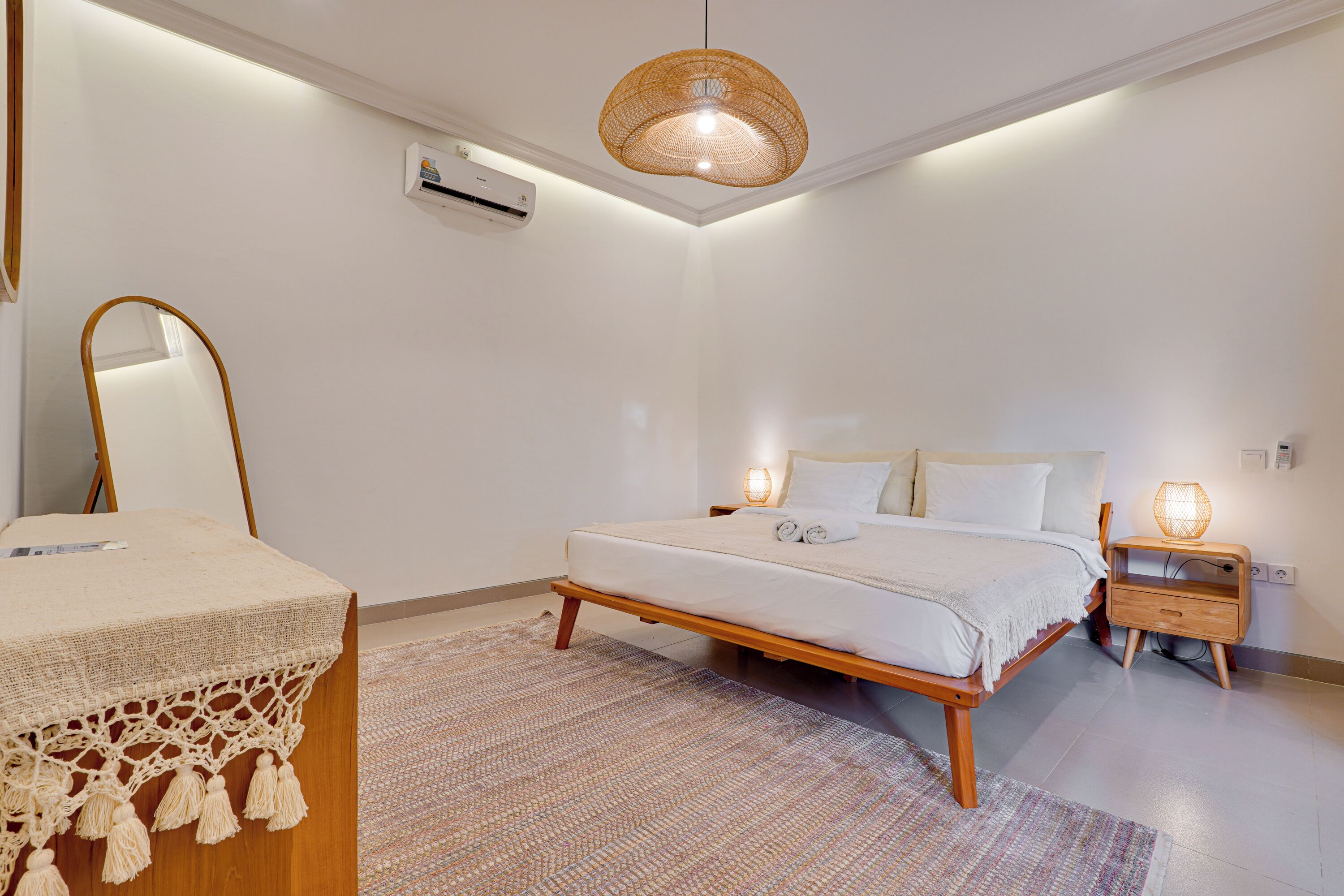 A bedroom with a bed, bedside table, lamp, air conditioning unit, and a hanging light fixture.