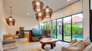 A modern living room with a large TV, sofa, and dining area. - Villa Aura Canggu (Canggu)