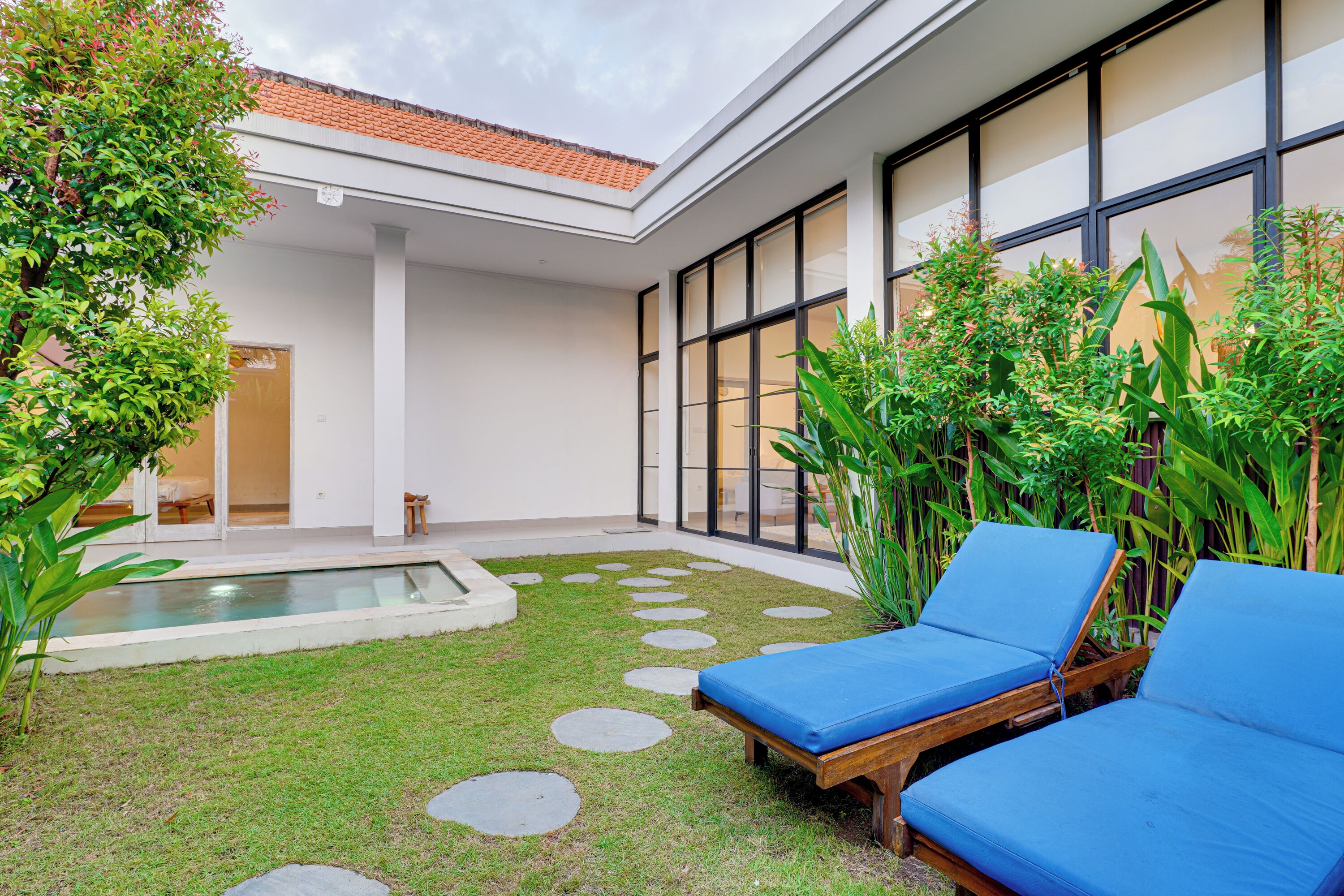 A modern outdoor area with a pool, lounge chairs, and a covered patio.