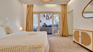 A bedroom with a bed, a bedside table, a lamp, a wardrobe, and a view of the living area through a glass door. - Villa Aura Canggu (Canggu)