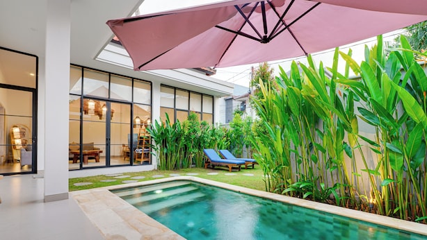 A modern pool area with a clear pool, lounge chairs, and a large umbrella. - Villa Aura Canggu (Canggu)