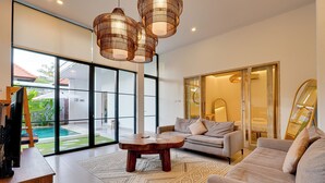 A modern living room with a sofa, coffee table, and large windows. - Villa Aura Canggu (Canggu)