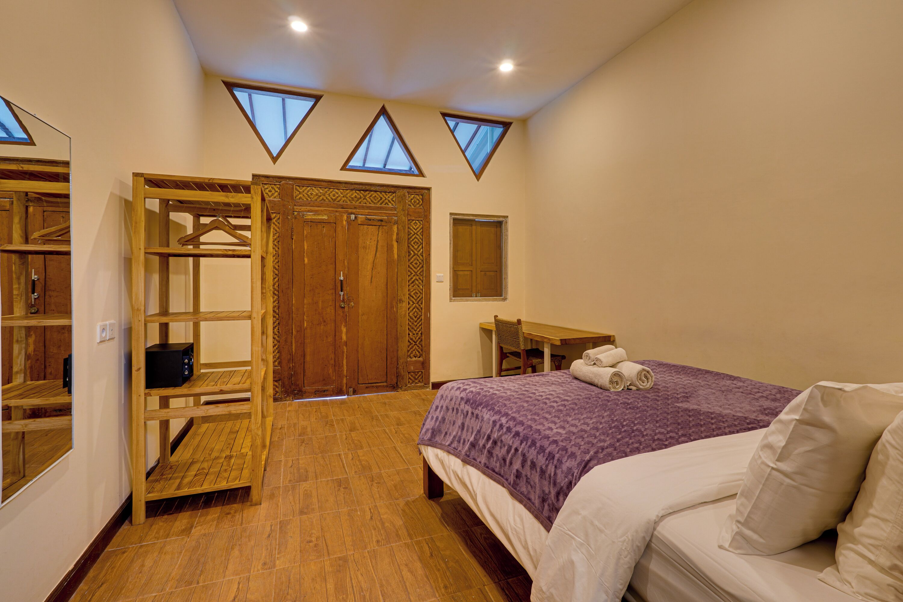Ein Schlafzimmer mit einem Bett, einem Holzschrank, einem Schreibtisch und einem Stuhl. Im Deckenbereich befinden sich Dachfenster.