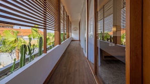 Un couloir avec des lambris en bois, un plancher en bois et une vue sur un bâtiment doté d’un toit rouge et de palmiers.