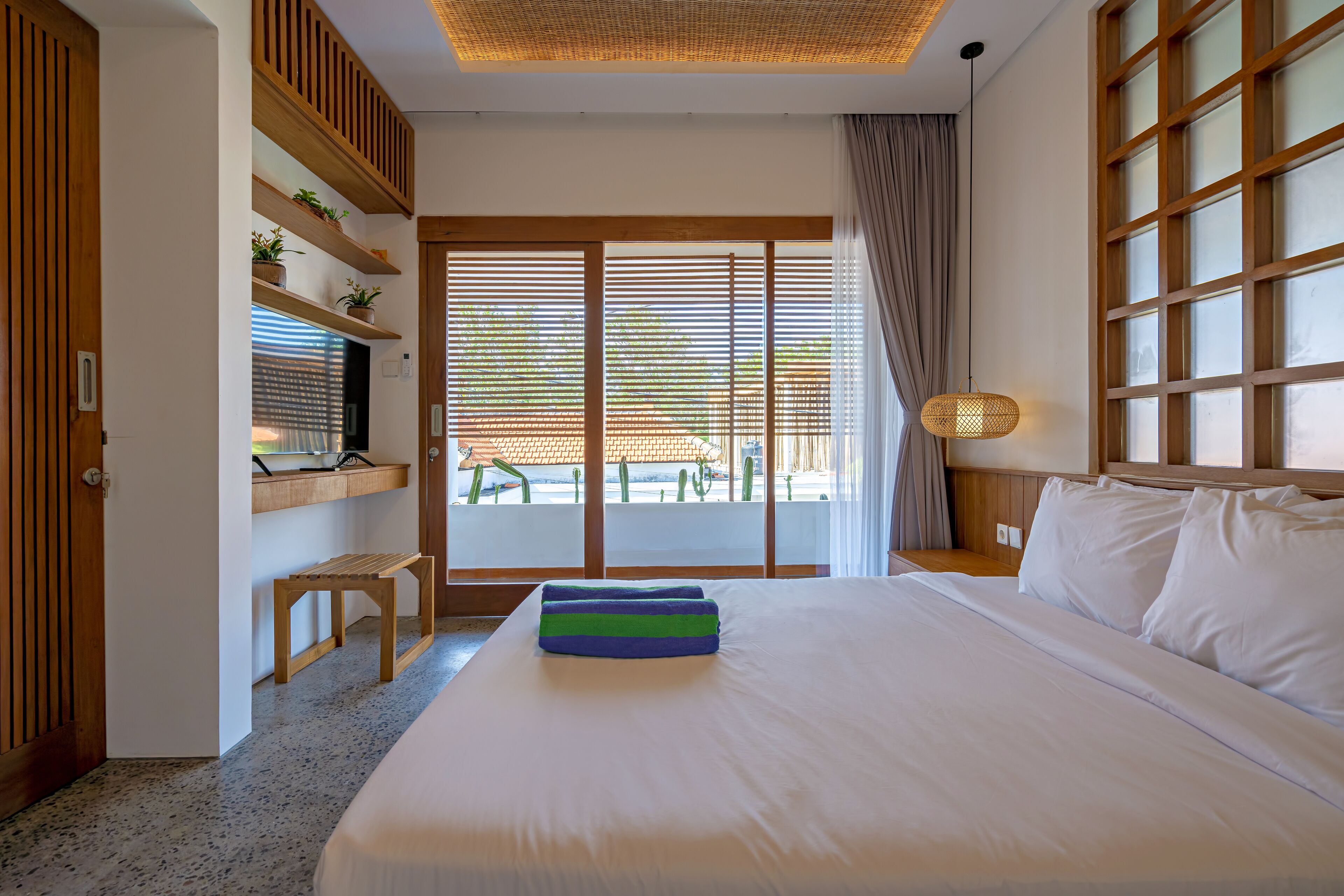 A hotel room with a large bed, wooden shelves, a desk, and a view of the outdoors.
