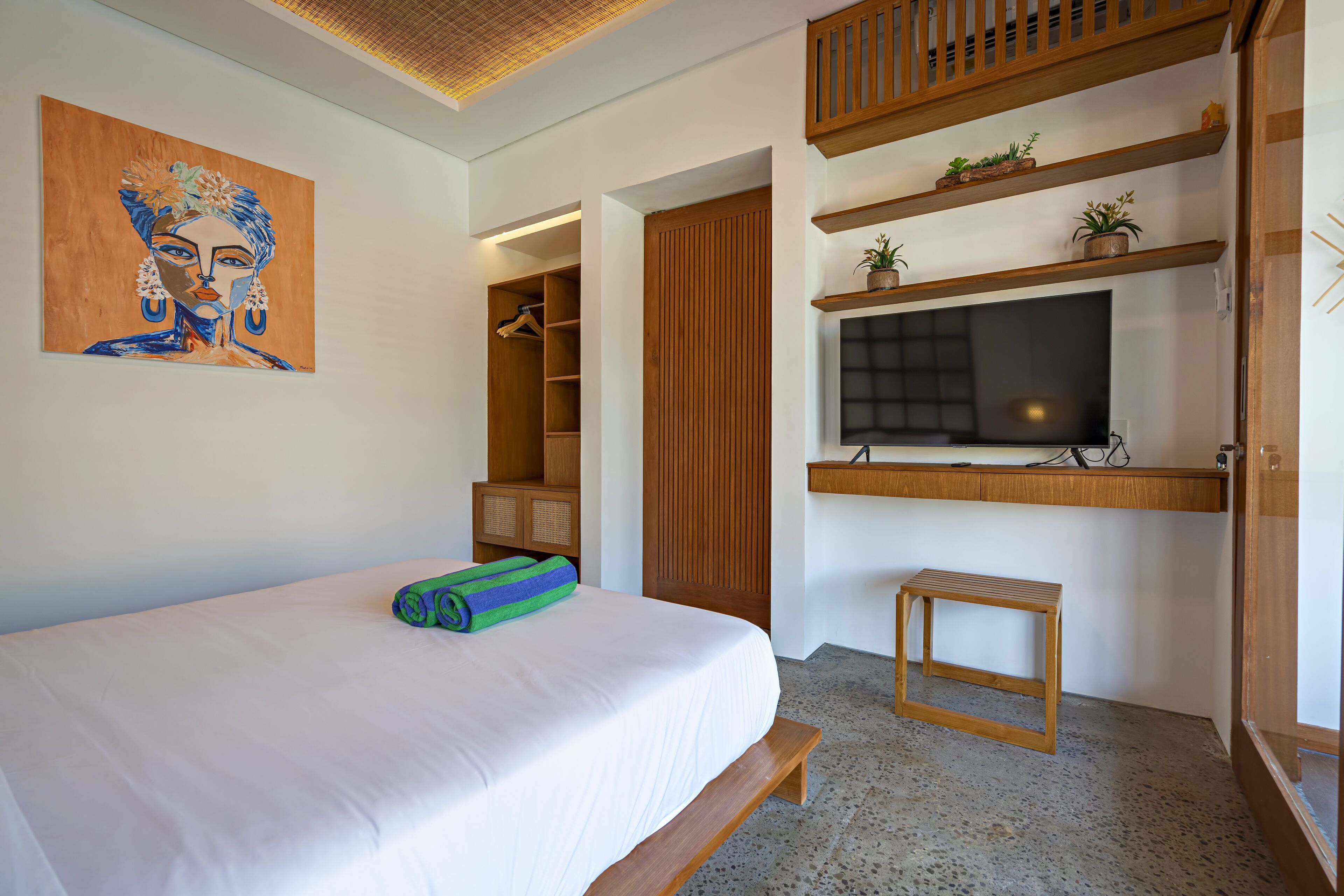 A bedroom with a bed, a painting, a wardrobe, a TV, and shelves with plants.
