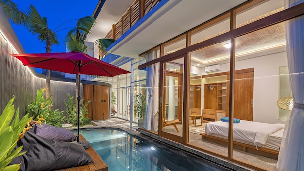 Une chambre d’hôtel moderne avec un mur en verre, une piscine et un parasol rouge.