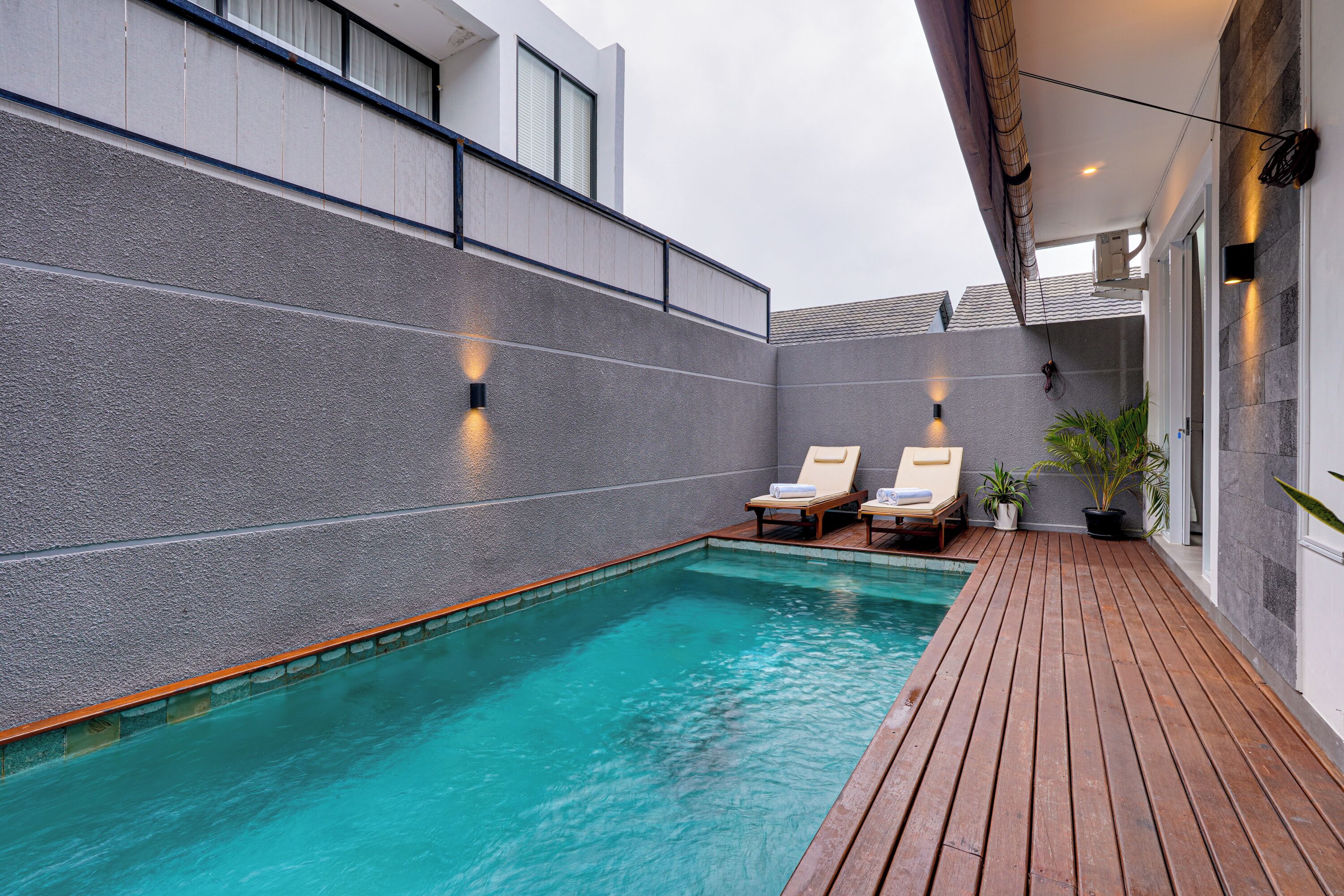 A swimming pool with wooden deck, lounge chairs, and potted plants.