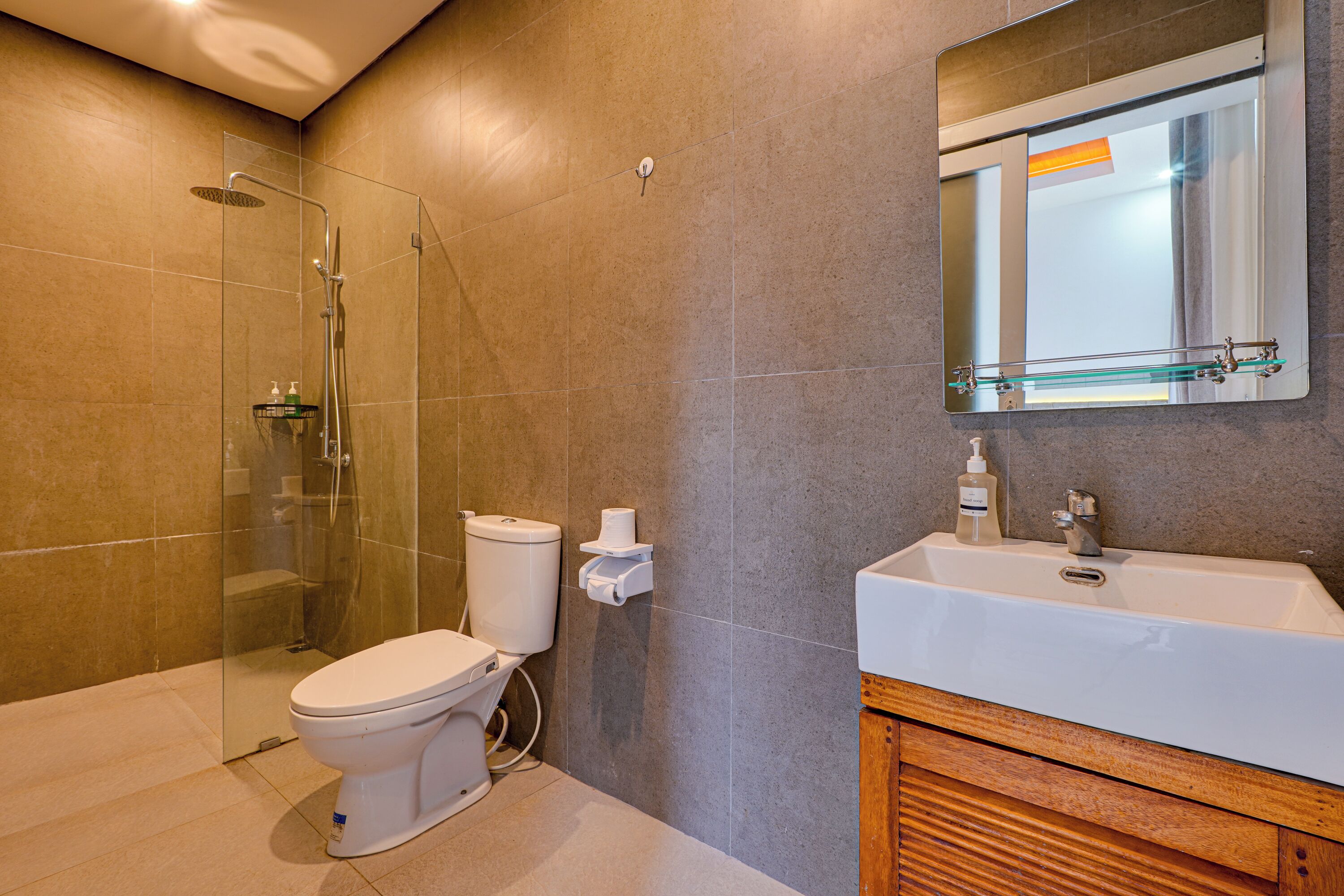 A modern bathroom with a glass shower enclosure, a toilet, a sink with a mirror above it, and a wooden vanity.