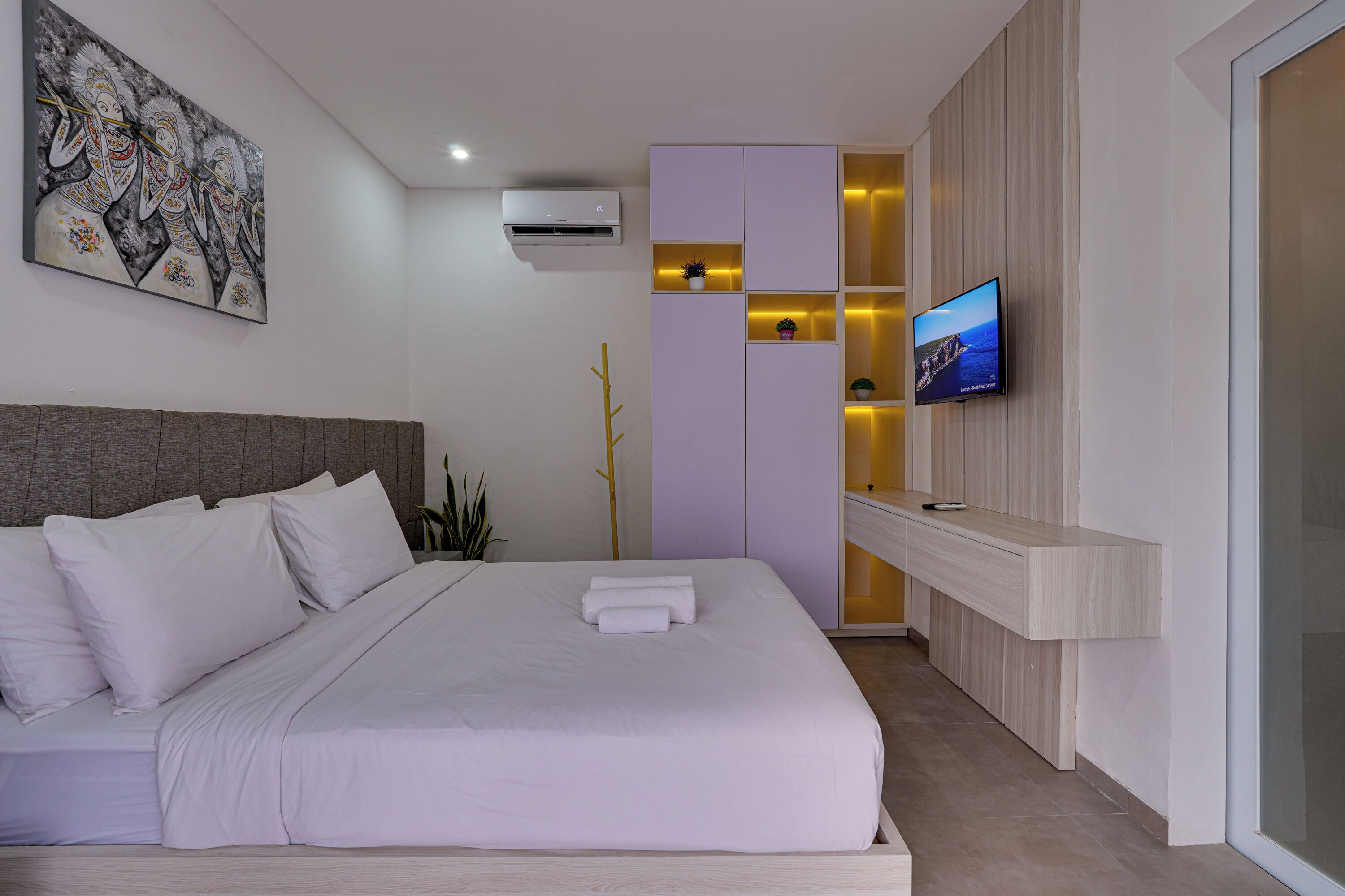 A modern hotel room with a large bed, a TV, a wardrobe, and a wall-mounted air conditioner.