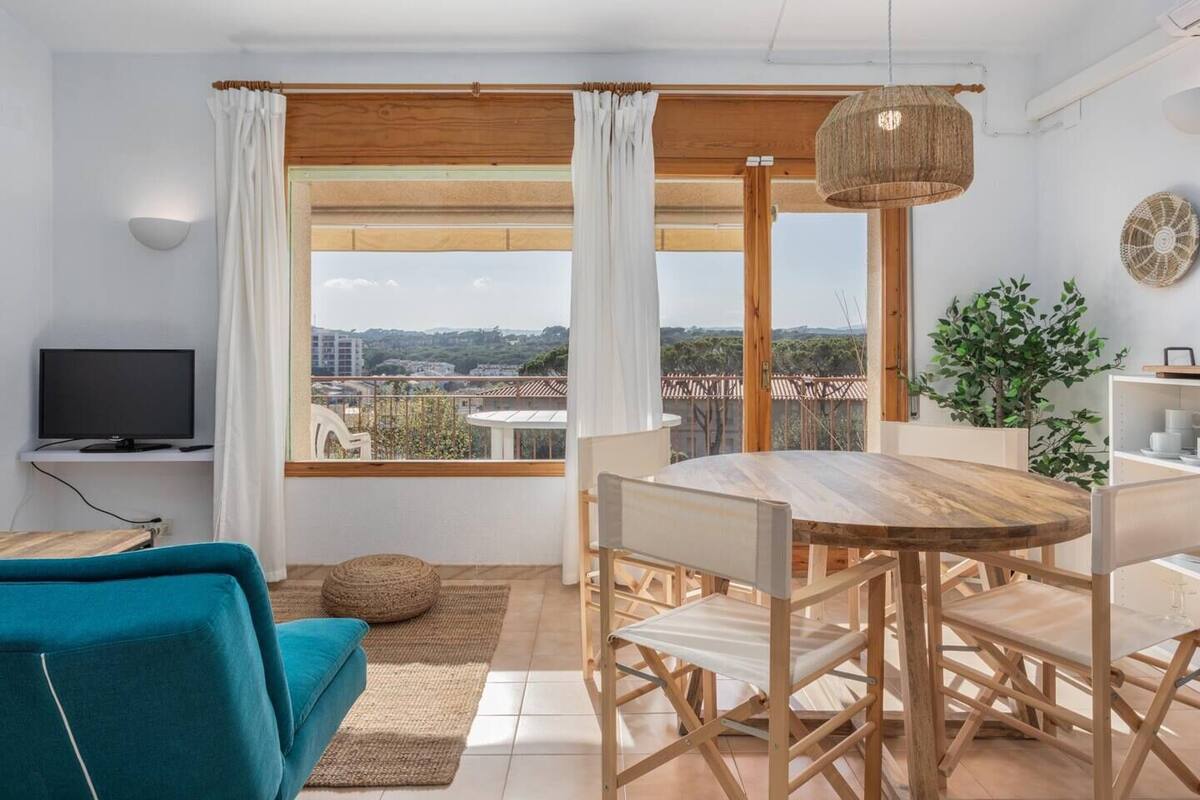 Ett modernt vardagsrum med ett matbord i trä, en turkosfärgad soffa och ett stort fönster med utsikt över staden.