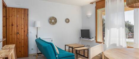 A modern living room with a teal sofa, wooden furniture, a TV, and a large window with curtains.