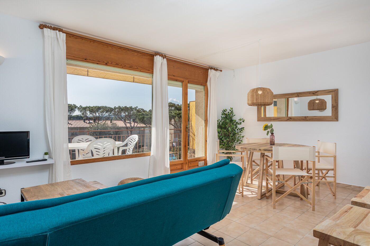 Una habitación con un ventanal grande, televisor, una mesa de comedor con sillas y un sofá color turquesa.