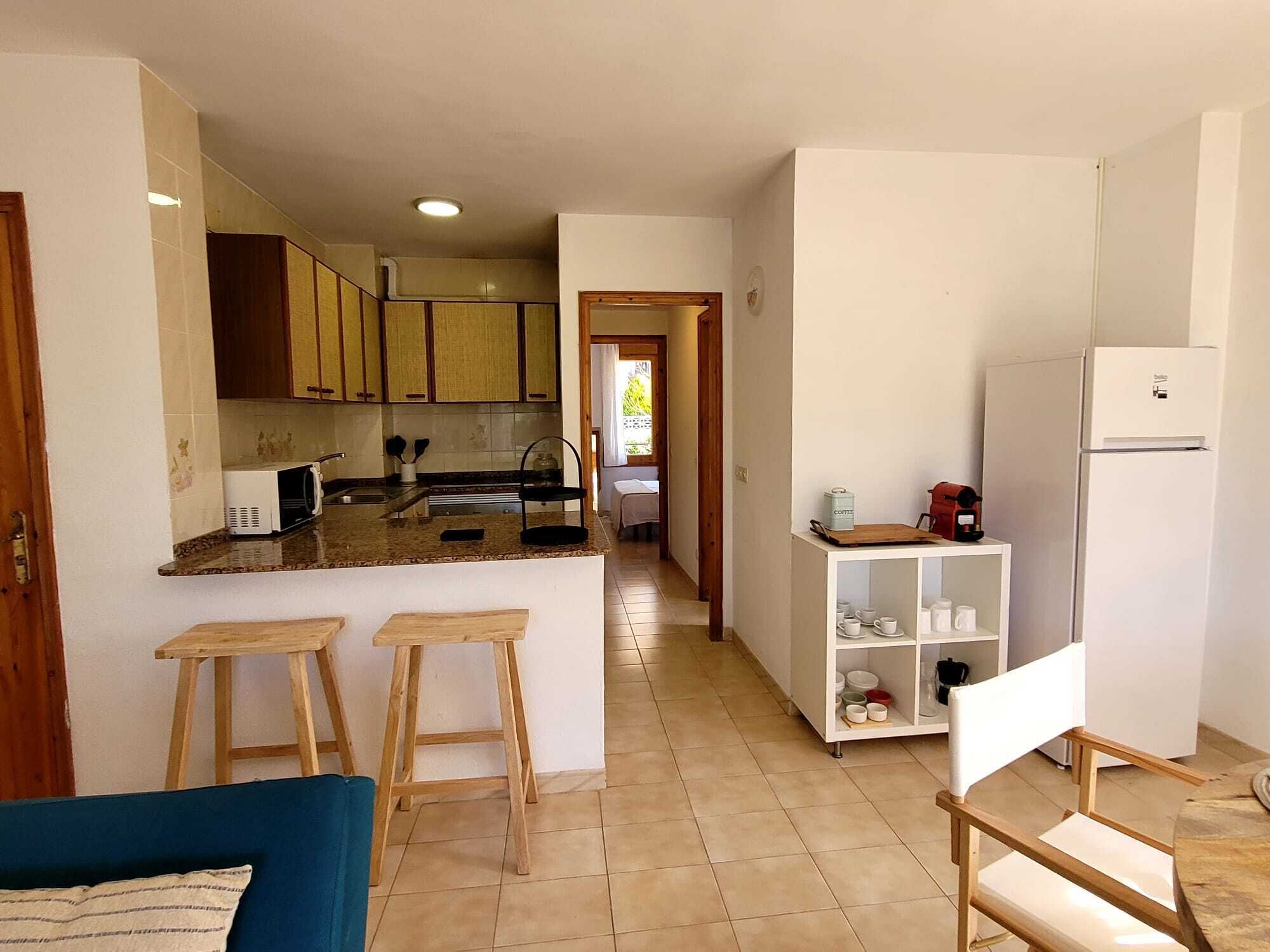 Una cocina compacta con una isla central, taburetes de madera, una estación de café y un refrigerador.