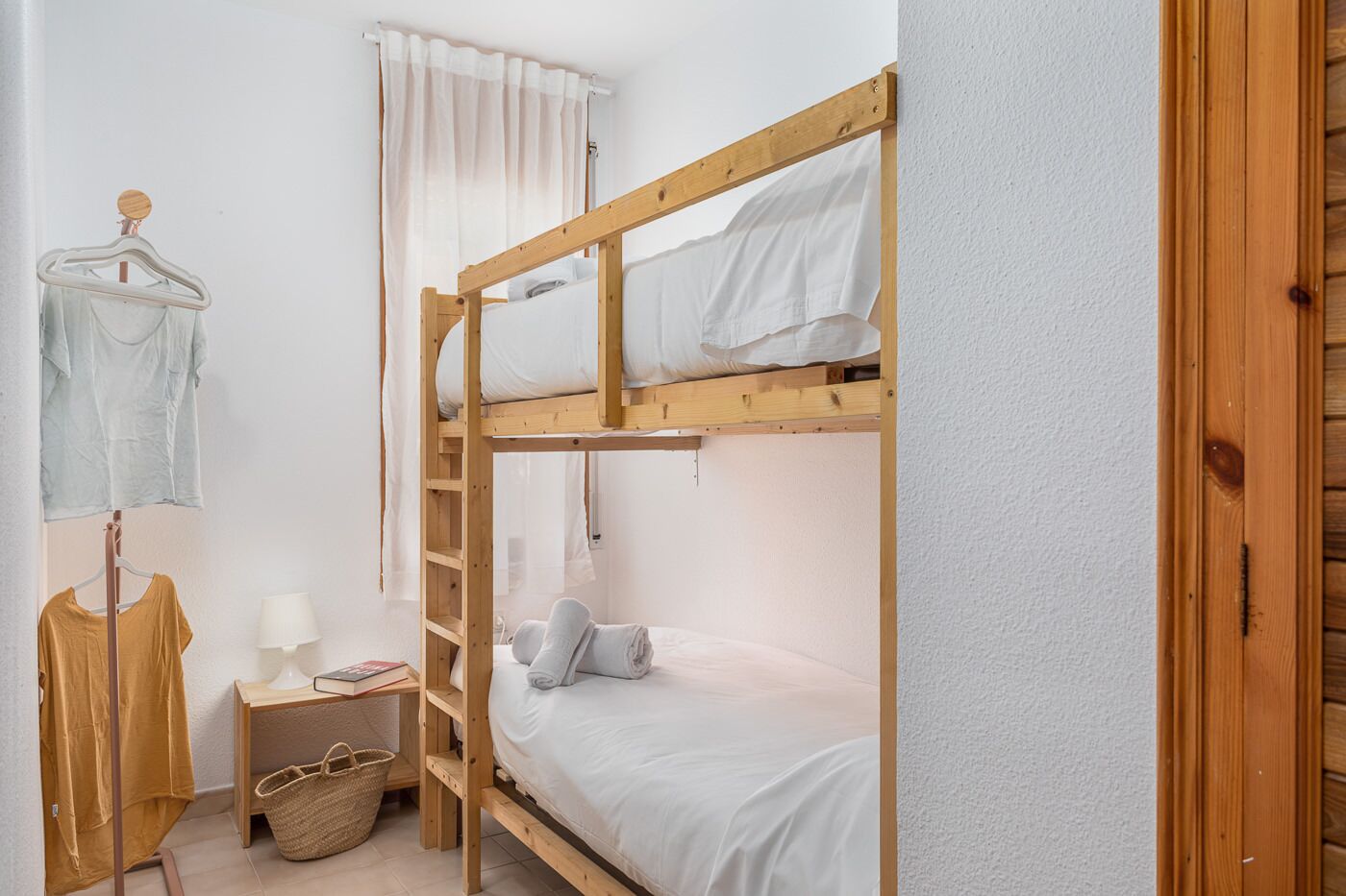 Quarto com beliche de madeira, mesa de cabeceira com abajur e um cabideiro.