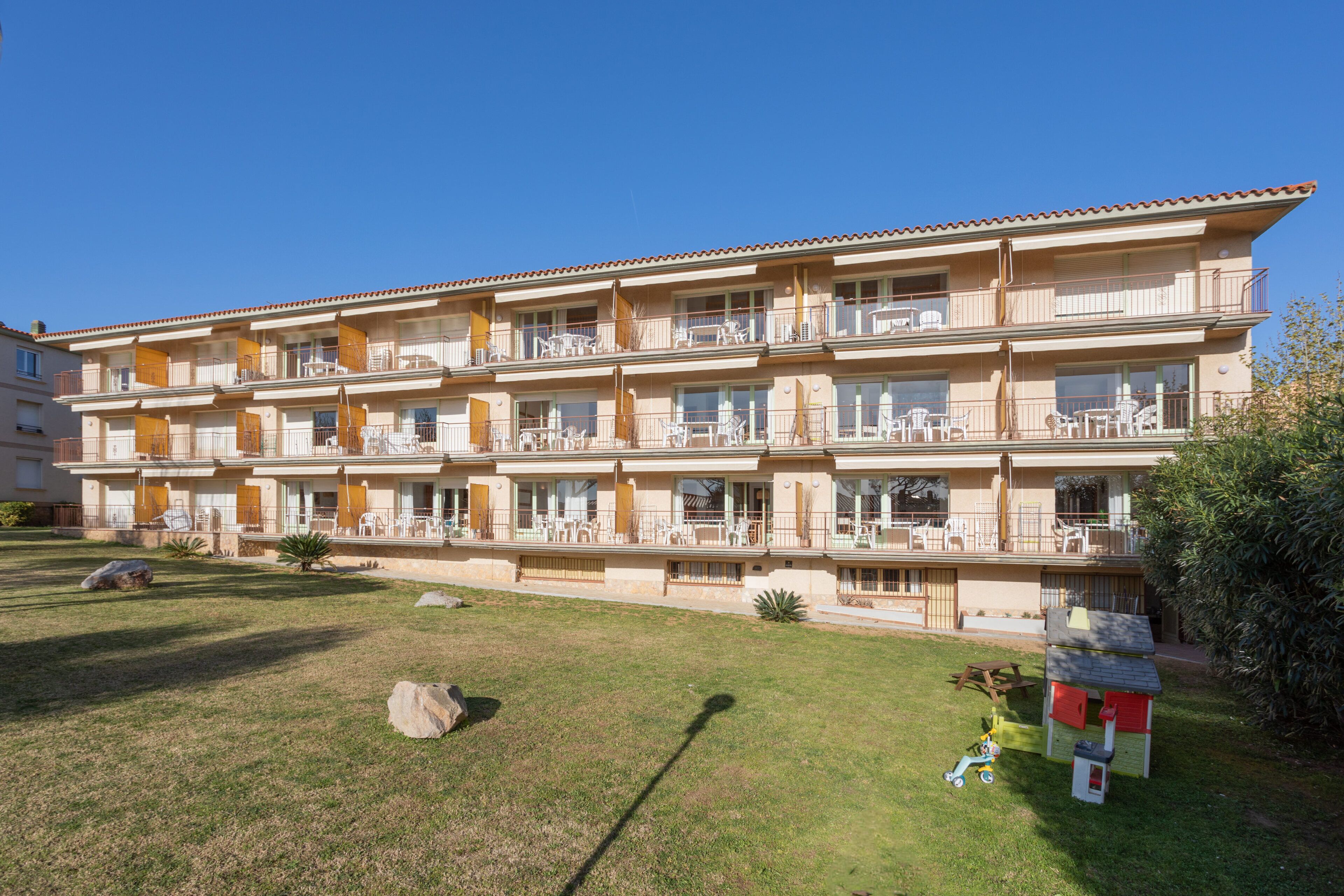 A multi-story hotel with balconies, a grassy lawn, and a children's play area.