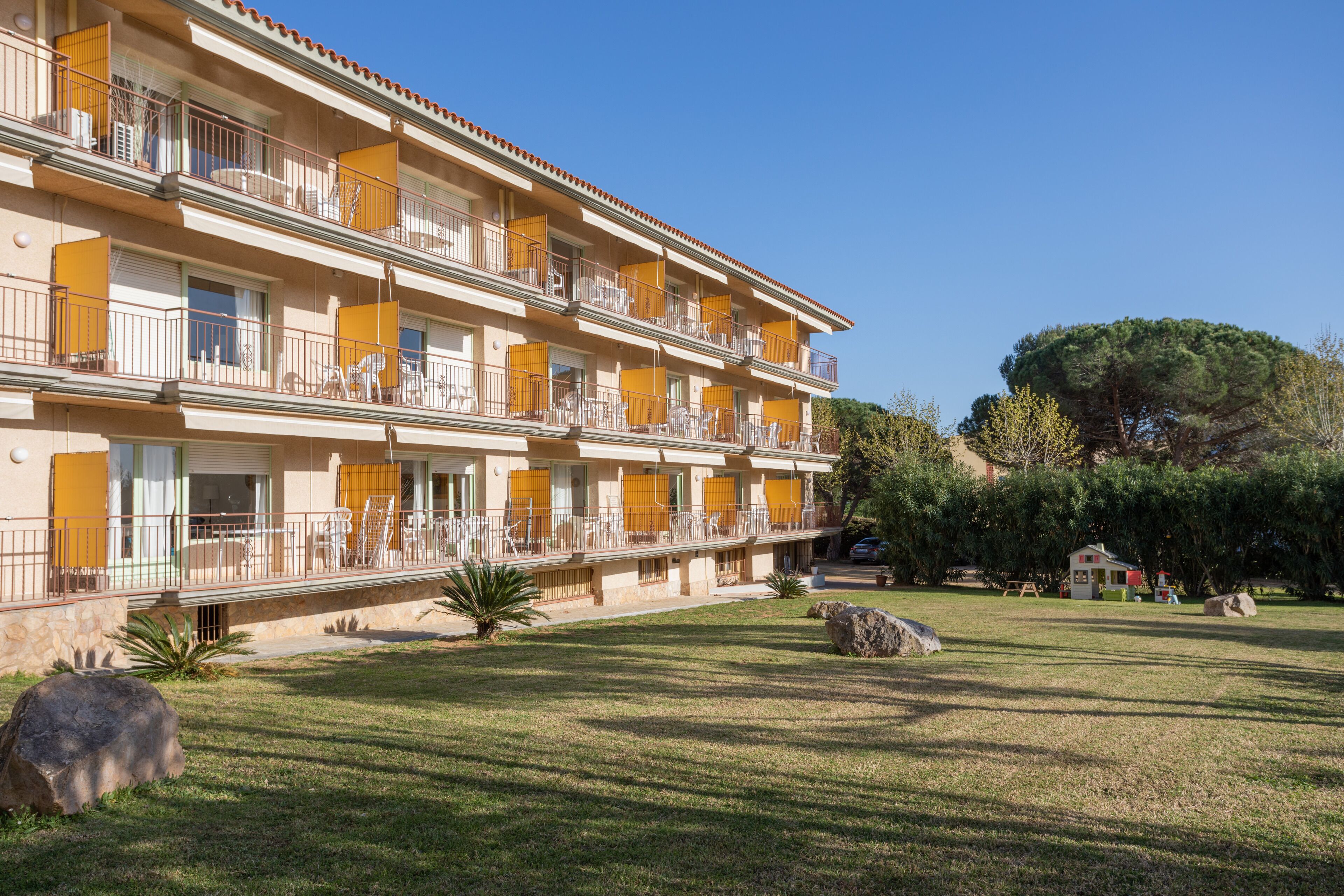 A multi-story hotel with balconies, a well-maintained lawn, and a large tree in the background.