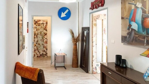 Un pasillo con un cartel indicador, una puerta con papel tapiz estampado, una pequeña mesa con un florero y una obra de arte colgada en la pared.