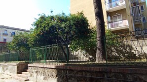A residential building with a beige exterior, a tree with orange fruits, and a green metal fence. - Room with private bathroom - Brown (Napoli)