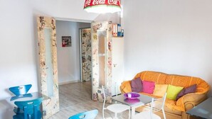 A living room with a sofa, chairs, a coffee table, and a refrigerator covered in stickers. - Room with private bathroom - Brown (Napoli)
