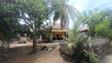 A courtyard with a building featuring a thatched roof entrance, surrounded by trees and plants.