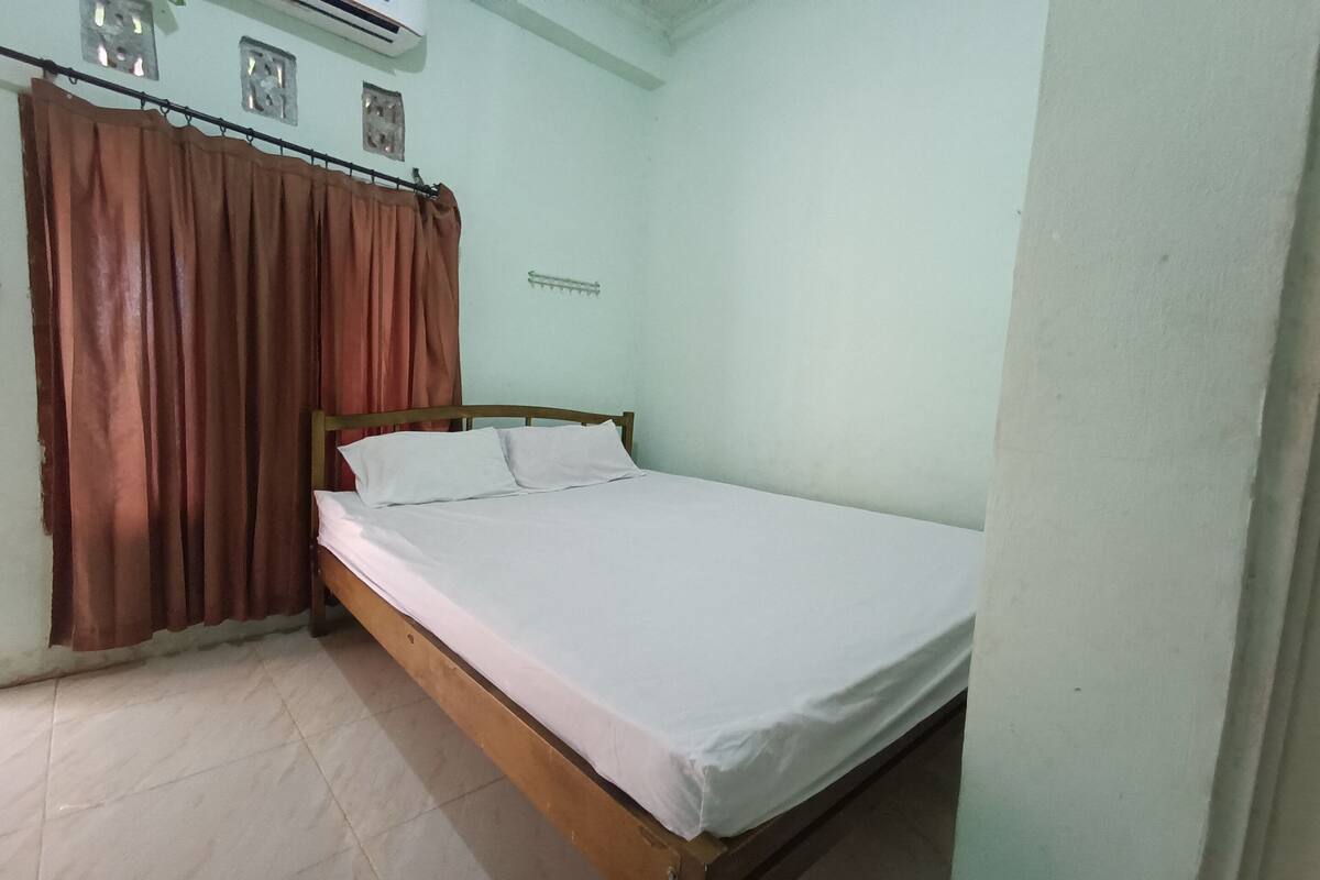A single-bed room with a wooden frame, white bedding, and brown curtains.