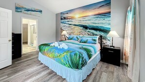 Un dormitorio con un mural de playa, un ventilador de techo y una cama con edredón de motivos tropicales.
