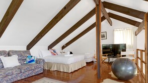 A cozy loft bedroom with a wooden ceiling, a sofa, a bed, a TV, and exercise equipment.