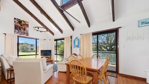 A spacious living area with a wooden dining table and chairs, a sofa, and a television.