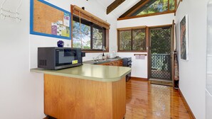 A kitchen with a central island, wooden cabinets, a microwave, and a window overlooking a balcony.