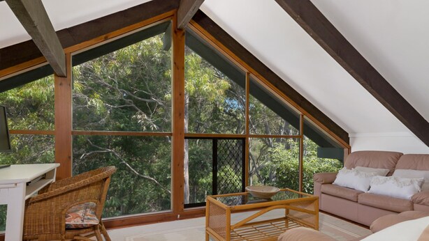A cozy attic room with a large window, a wicker chair, a sofa, and a small table.