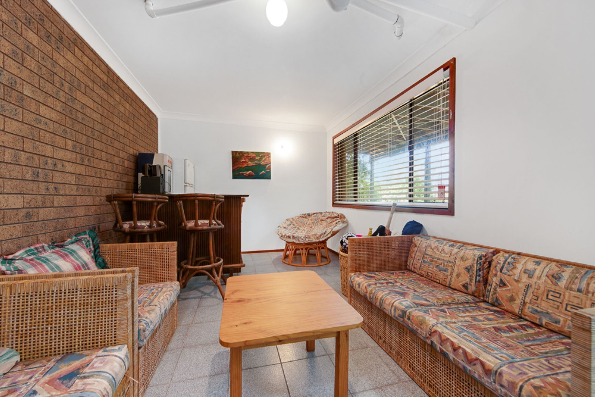 Una habitación acogedora con muebles de mimbre, una mesa de madera y un gran ventanal con persianas.