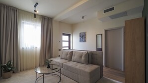 Uma sala de estar moderna com um sofá seccional, uma mesa de centro de vidro e uma janela grande com cortinas.