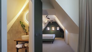 Um quarto de sótão moderno com janelas no teto, uma cama, uma mesinha de cabeceira com uma planta e um pequeno espaço de trabalho.