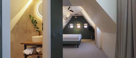 A modern attic bedroom with a skylight, a bed, a bedside table with a plant, and a small desk area.