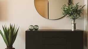 Un interno moderno con uno specchio tondo appeso al muro, un consolle in legno scuro con sfere decorative e una pianta in vaso.