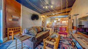 A cozy living area with a leather sofa, wooden coffee table, and patterned rugs. A 'WELCOME' sign is visible on the wall.