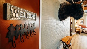 Ein rustikales Interieur mit einem 'WELCOME'-Schild, einer Wandskulptur aus Metall und einem aufgehängten Fellmantel.