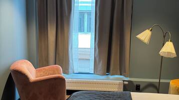 Una habitació d'hotel amb un llit, una cadira, un escriptori, una làmpada i una finestra amb cortines.