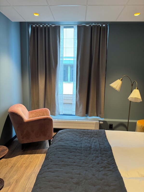 A hotel room with a bed, a chair, a desk, a lamp, and a window with curtains. - Hotell Sillen (Lysekil)