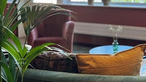 A room with a sofa, a chair, a window with a view of the sea, and potted plants. - Hotell Sillen (Lysekil)